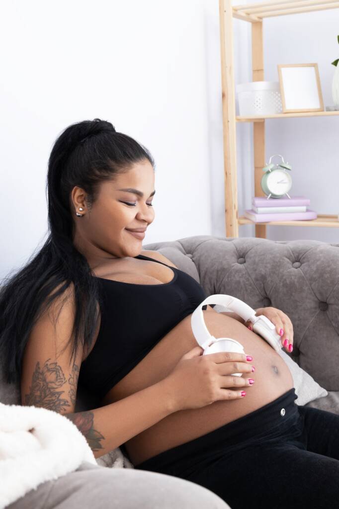 Pregnant African American woman with headphones on yellow background.